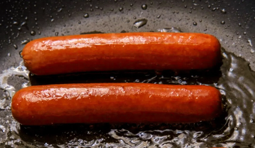 Riscaldare gli hot dog in una padella nera con olio